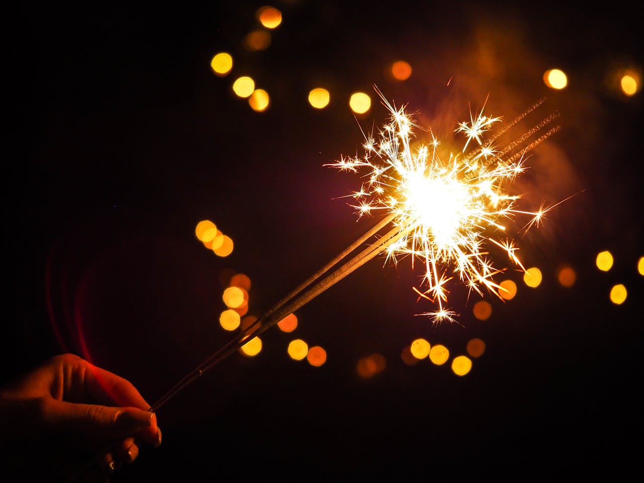 programs-01 A vibrant sparkler glowing against a dark background with bokeh lights, symbolizing celebration.