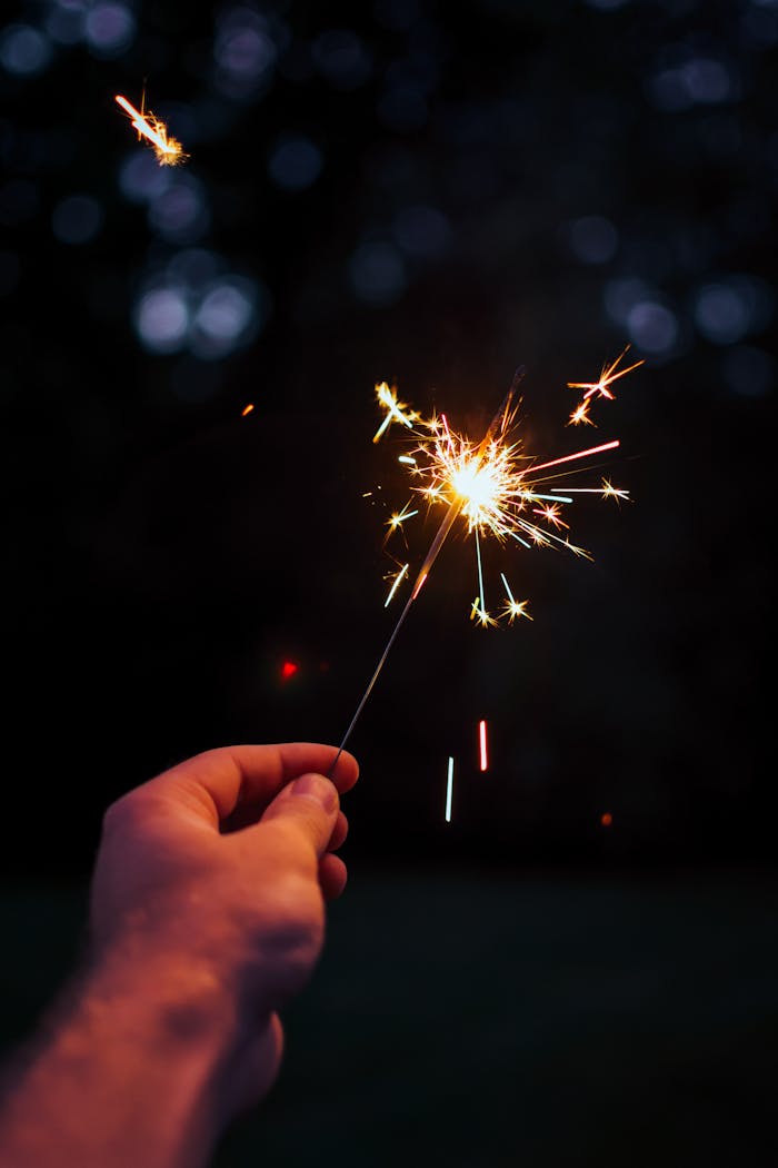 gallery-img-03 A person holding a bright sparkler outdoors in a festive night setting.